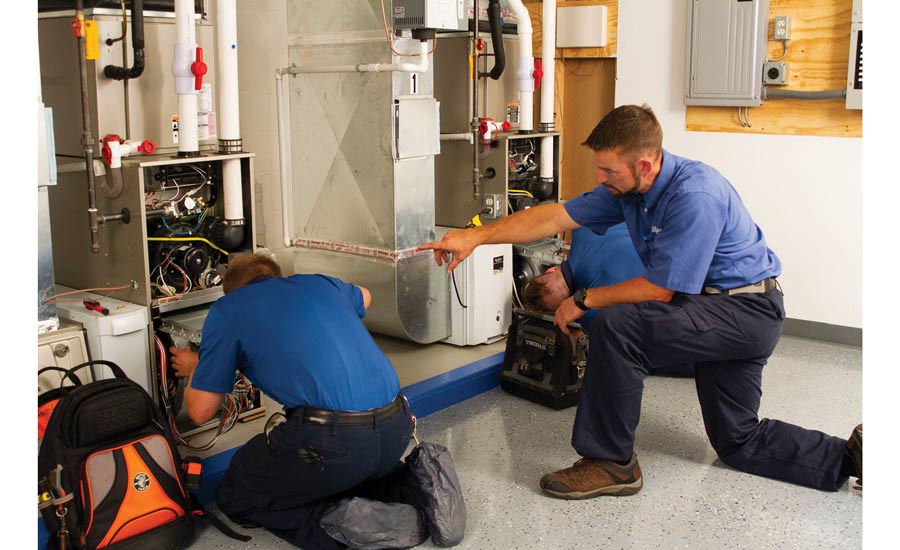 Two HVAC technicians performing work on a furnace in a garage