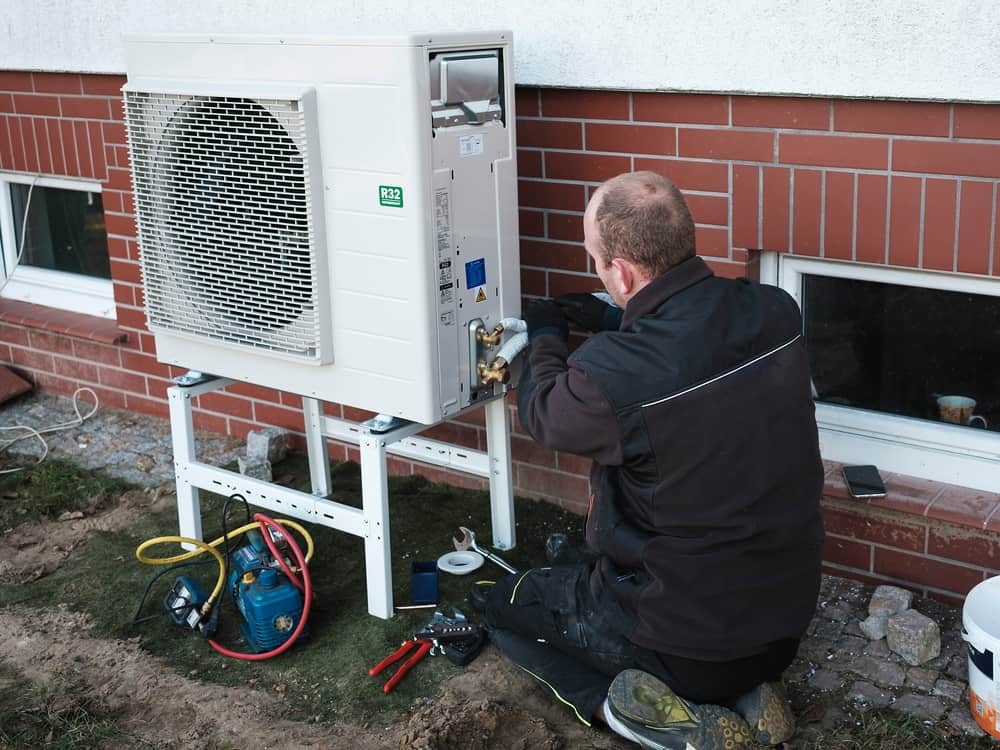 HVAC technician using a power drill to secure a part of a heat pump on exterior of a home