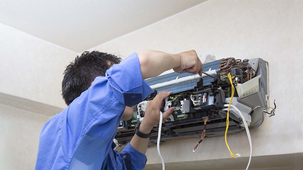 HVAC technician with screwdriver performing service on the internal workings of a mini-split system