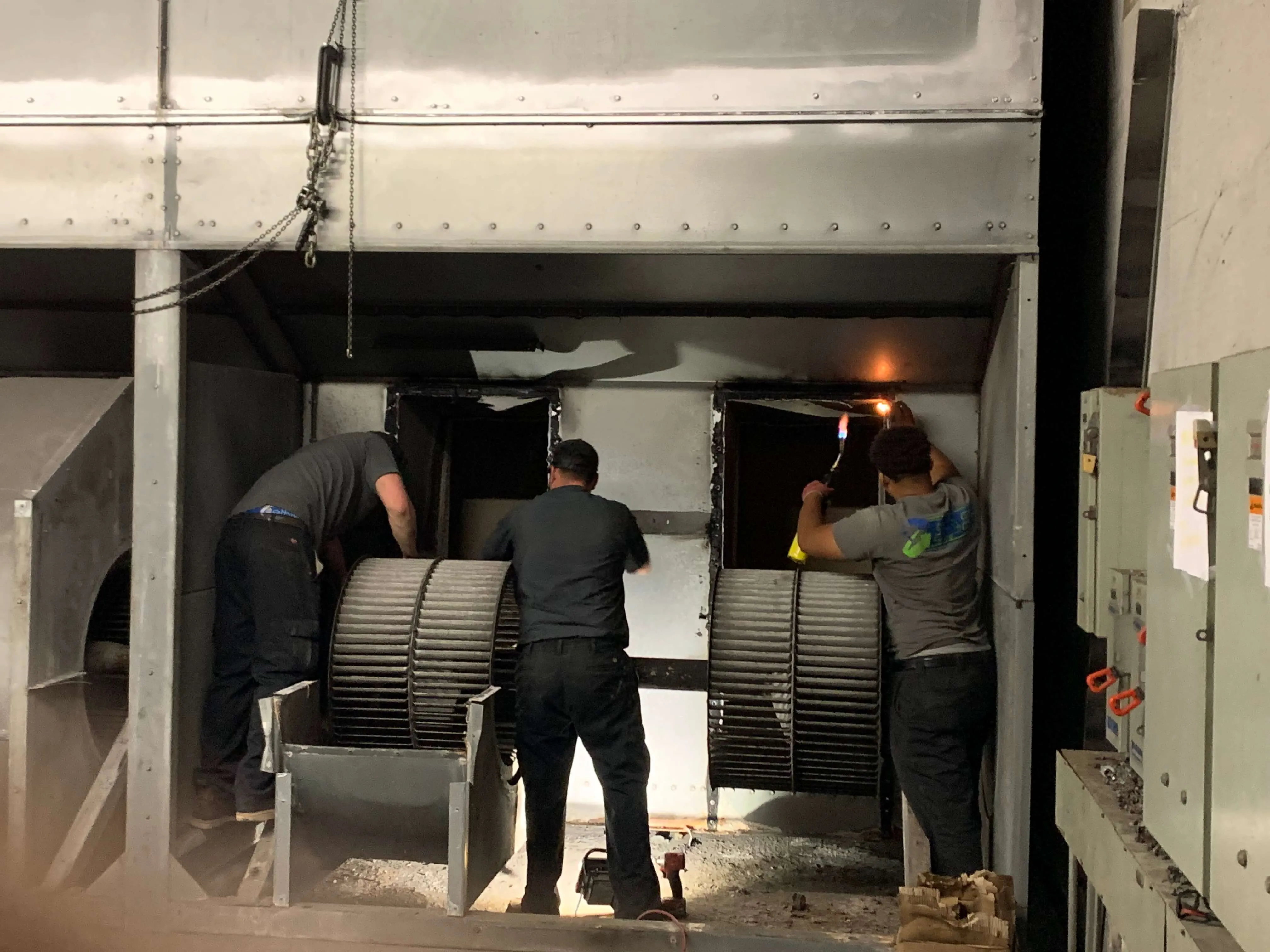 Workers repairing large industrial fans inside a mechanical equipment room
