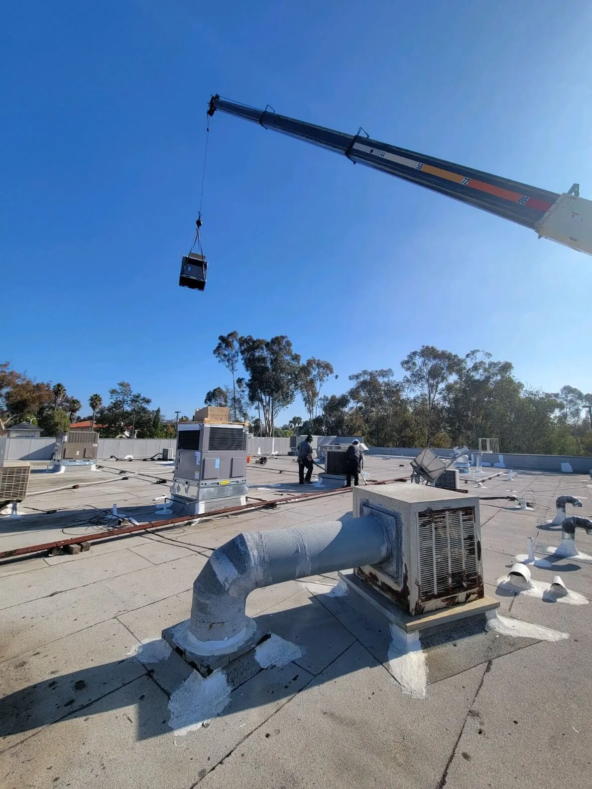 Crane lifting HVAC unit on a flat roof with workers and equipment