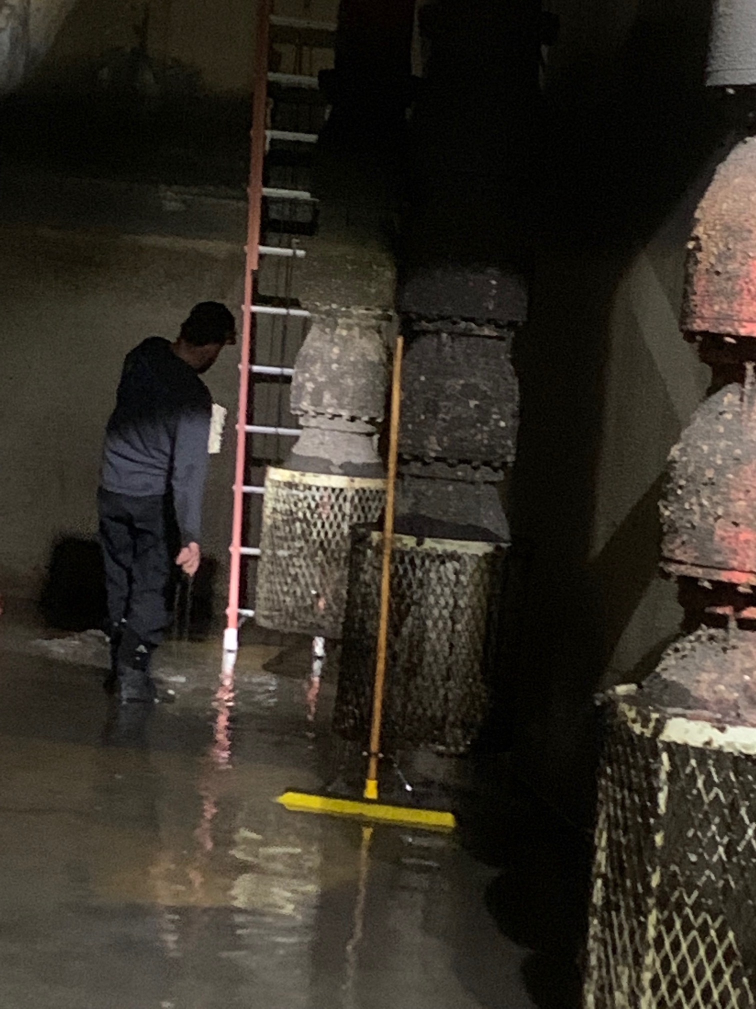 Worker with ladder and broom cleaning flooded industrial area at night