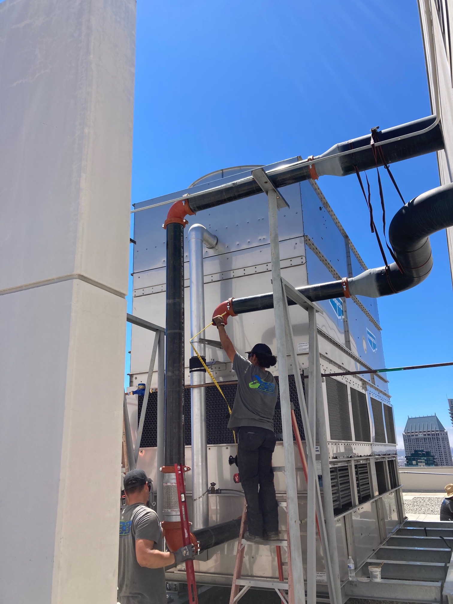 Technicians inspecting industrial cooling system on rooftop under blue sky