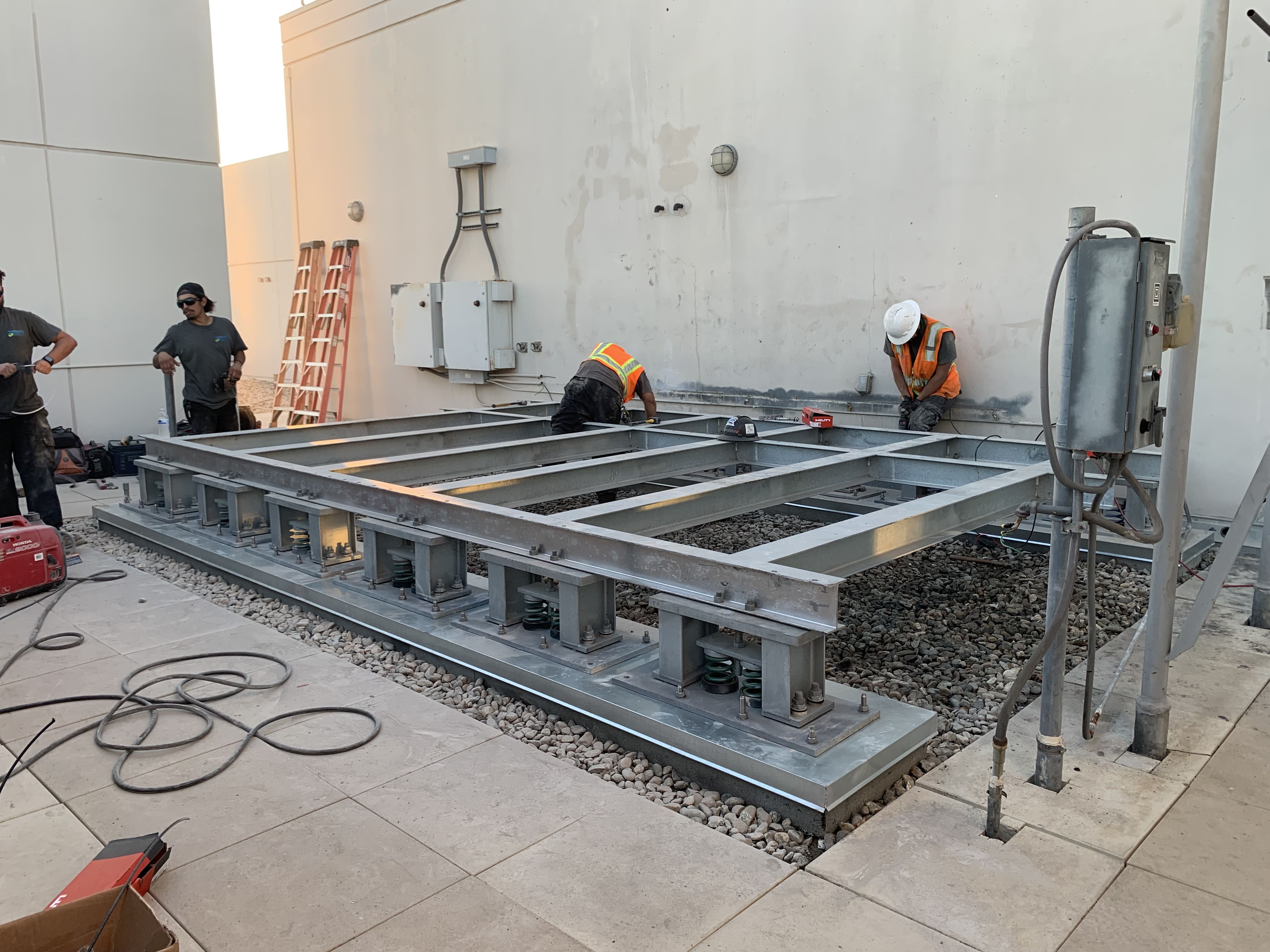 Construction workers installing large metal frame on rooftop with spring supports