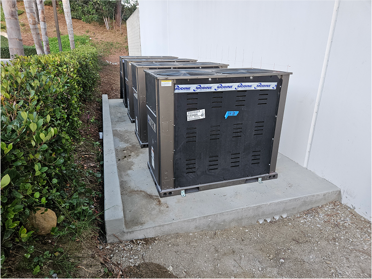 Large black HVAC units installed on concrete pad near bushes and trees
