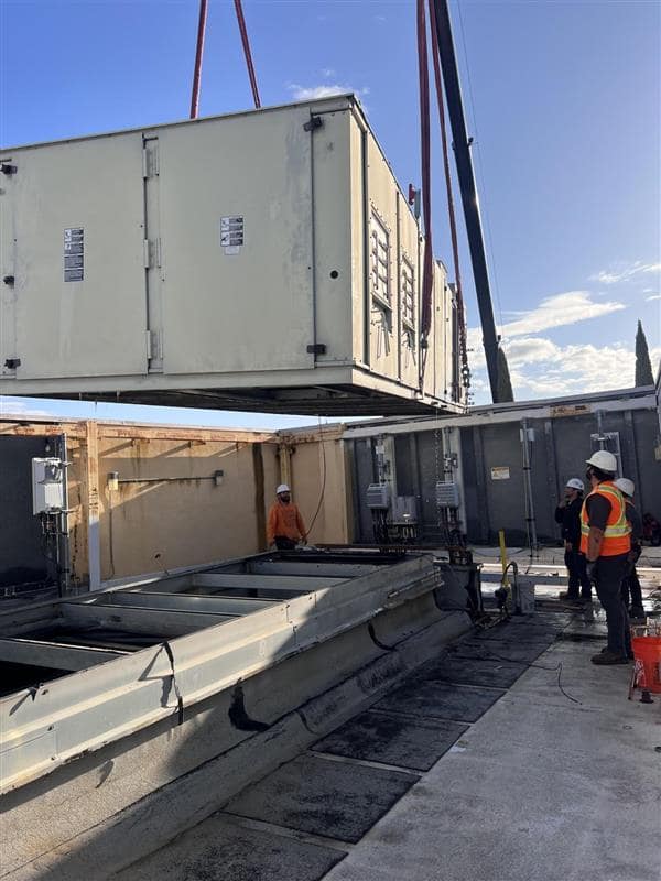 Construction workers using crane to lift large industrial equipment on site
