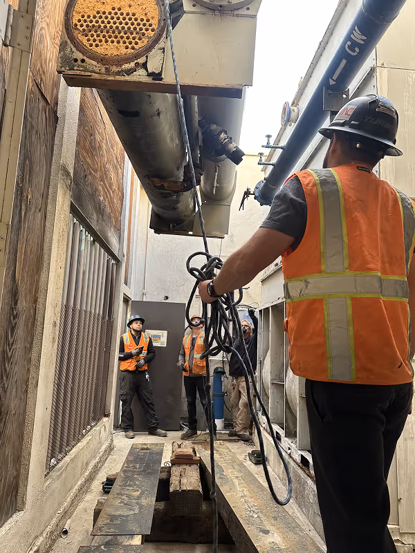 Construction workers in safety vests inspect industrial machinery and pipes