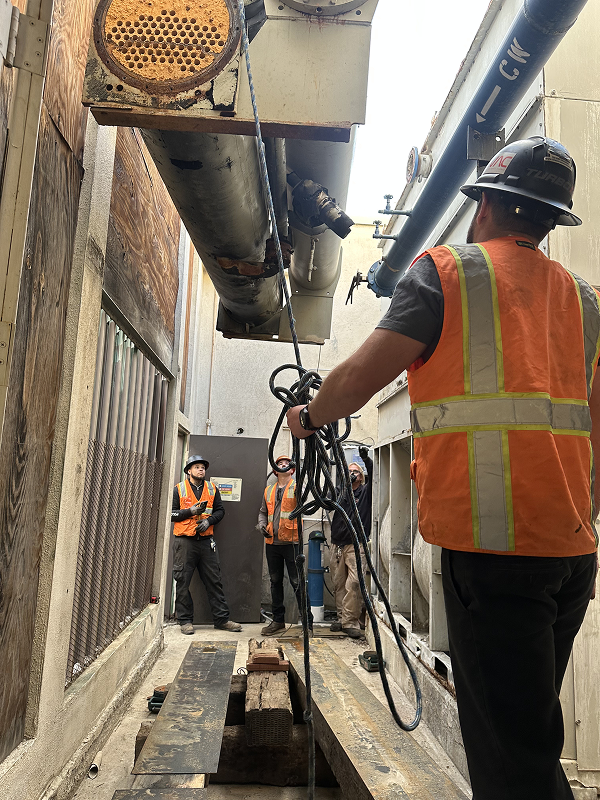 Construction workers in safety vests inspect industrial machinery and pipes