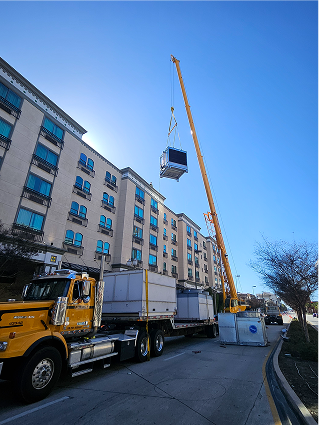 Yellow crane lifting shipping container near multi-story apartment building