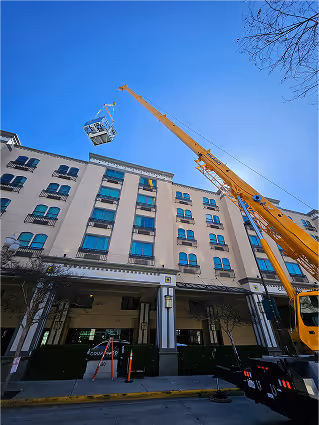 Yellow crane lifting equipment near modern white building with blue windows