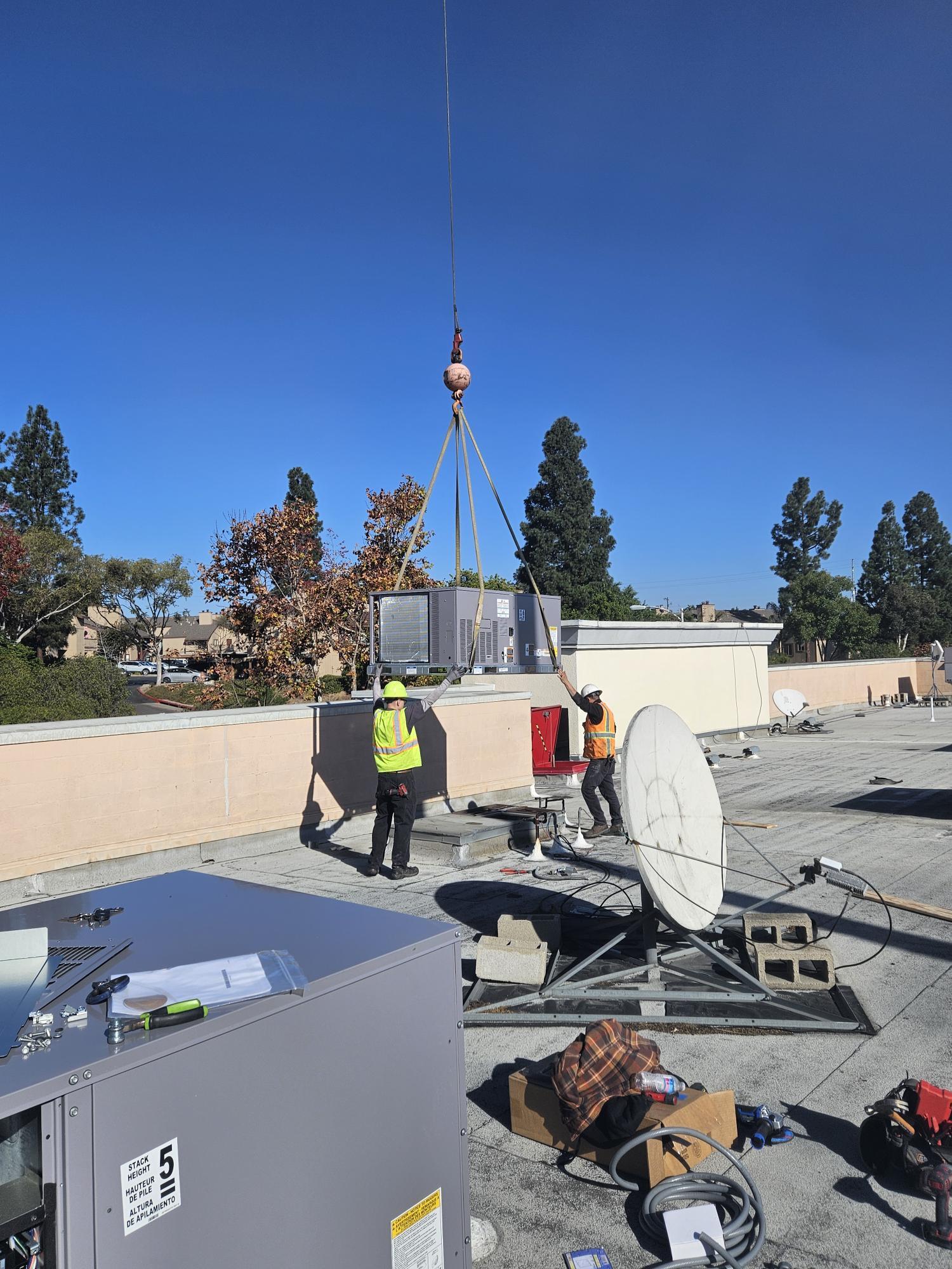 Workers using crane to install HVAC equipment on a rooftop