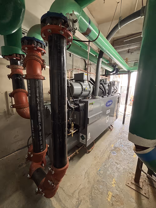 Industrial chiller in a mechanical room, featuring large green and black pipes.