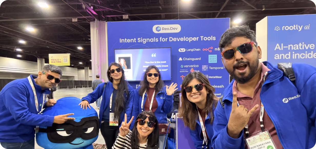 Reo.Dev team members posing with their mascot at the company booth during a technology conference.