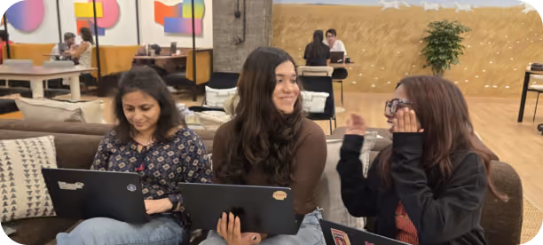 Three colleagues working together with laptops while discussing ideas in a collaborative office lounge.