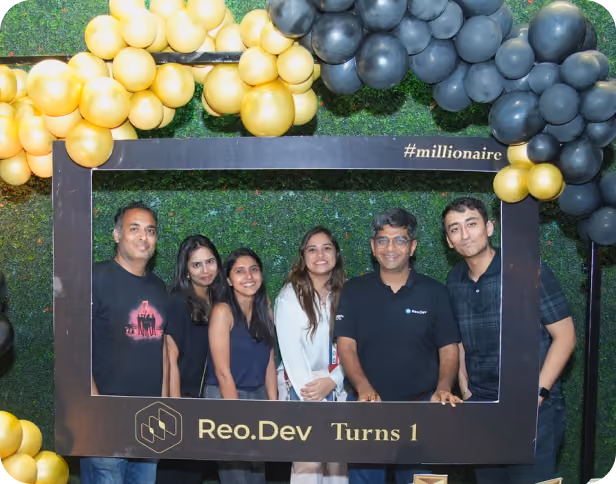 Six team members posing together inside a decorative photo frame during Reo.Dev's first anniversary celebration.