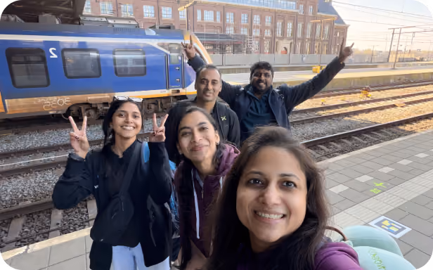Five colleagues smiling for a selfie on a train station platform while traveling together.