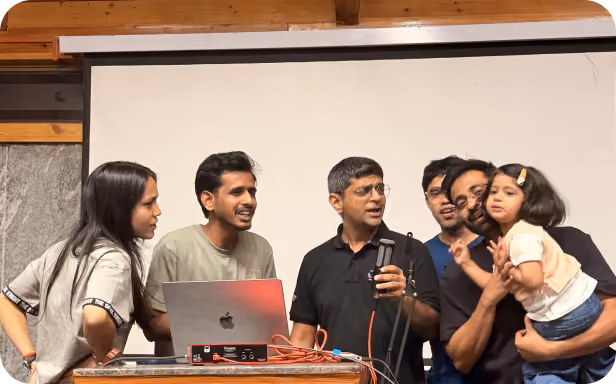 A group of colleagues gathered around a microphone during a karaoke session, with one team member holding a young child.