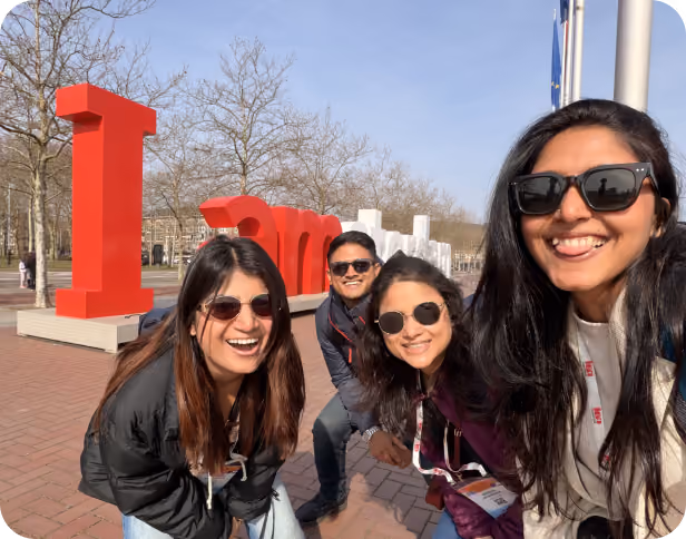 Four team members smiling in front of the iconic "I amsterdam" sign during an outdoor company trip.