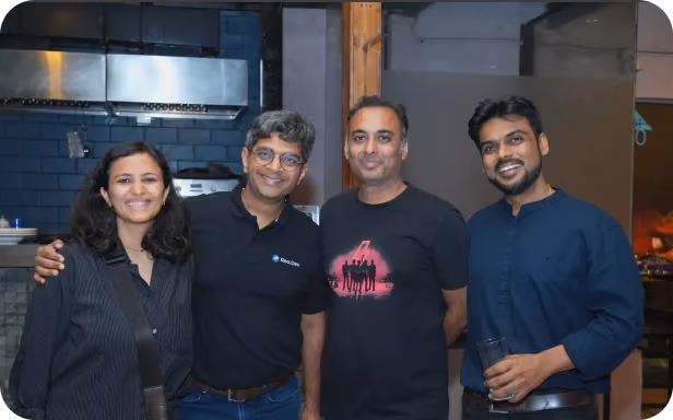 Four colleagues posing together and smiling at an indoor company networking or social event.