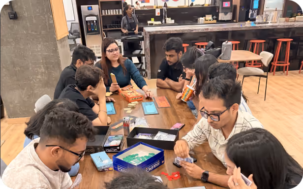 A group of colleagues gathered around a table playing board games during a team-building activity in a modern office lounge.