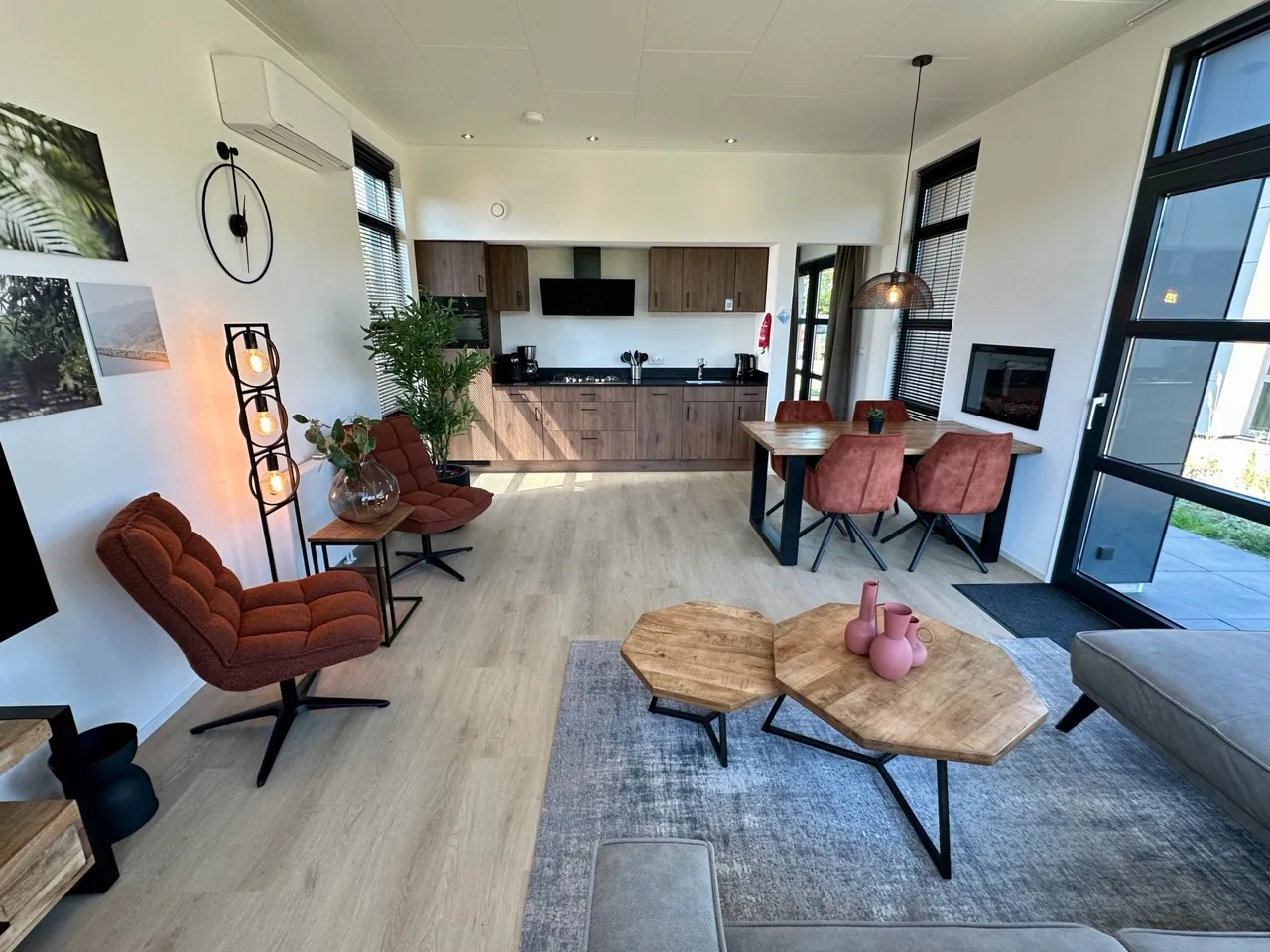 Offener Bereich mit Holz-Esstisch, Couchtischen, Bildern, Pflanzen, Fenstern und Küche im Hintergrund.