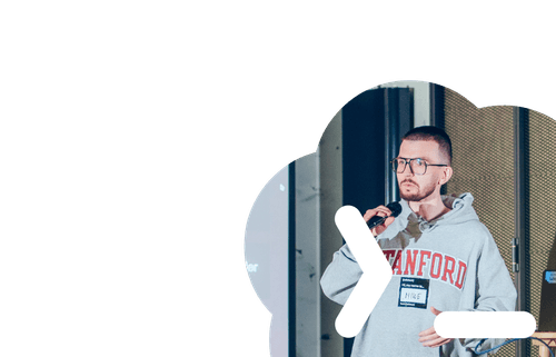 Man wearing glasses and a Stanford sweatshirt speaking into a microphone during a presentation.