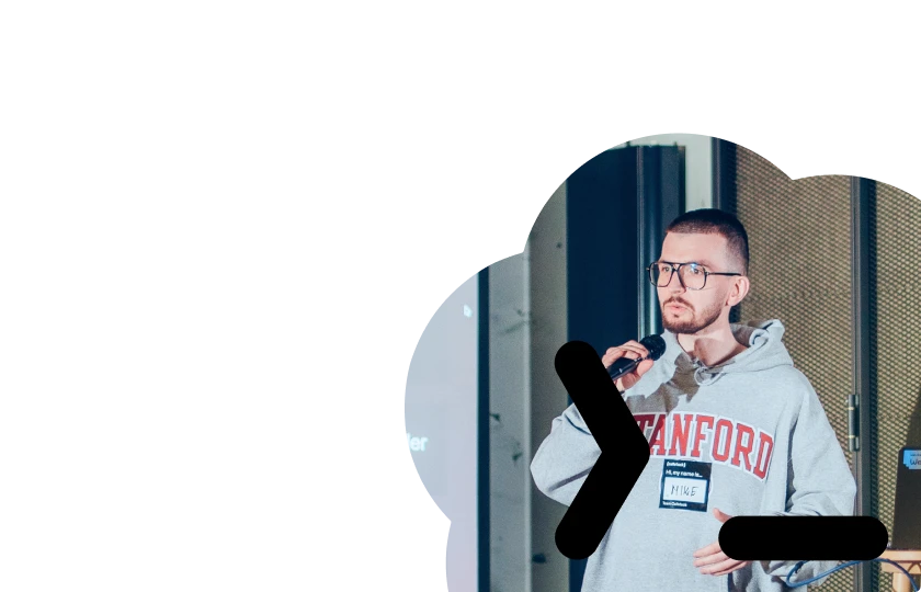 Man wearing glasses and a Stanford sweatshirt speaking into a microphone during a presentation.