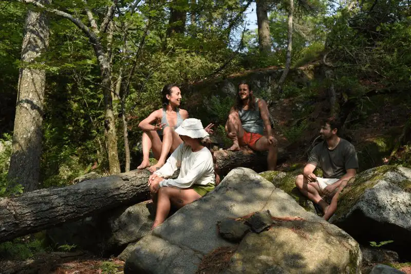 A group of people in summer clothes sitting on rocks and a log in a forrest