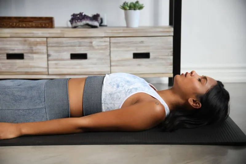 A woman laying down on a black yoga mat with her eyes closed