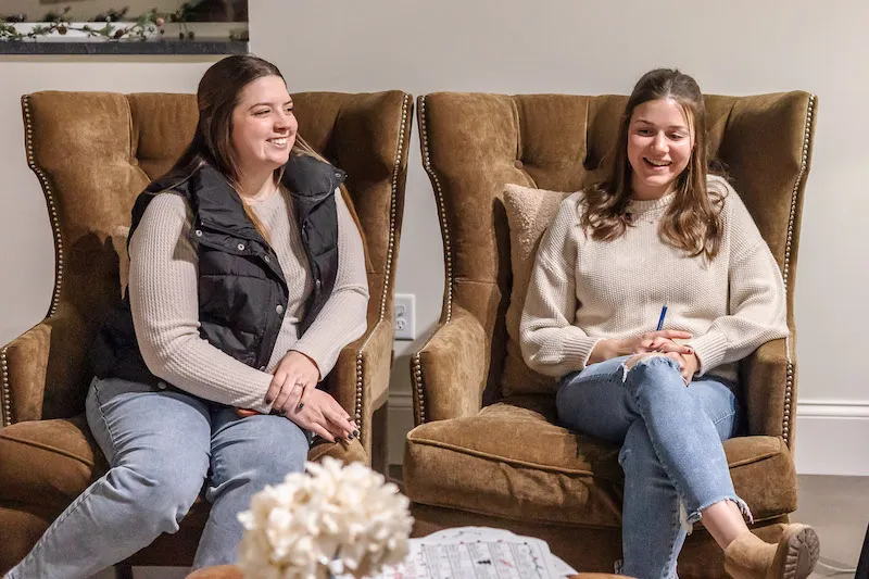 Two women sitting in cozy, large armchairs, smiling and chatting.