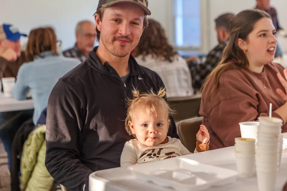 A father and his young child at a crowded table, smiling with food trays and cups.