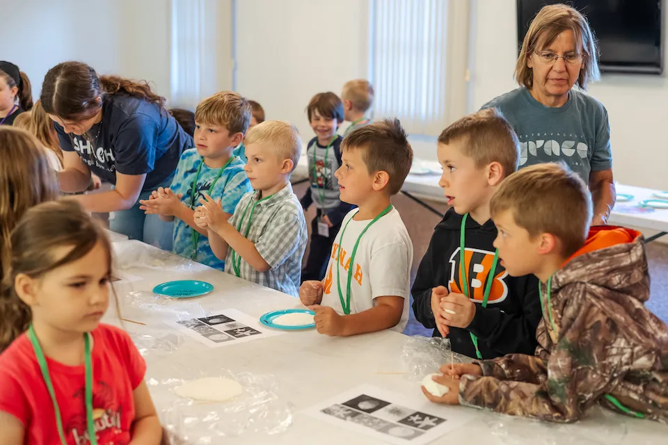 A group of young children at a table engaged in a craft activity, supervised by an adult.
