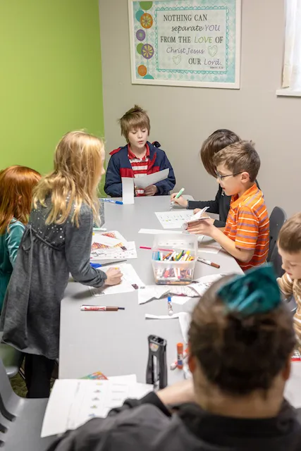 A group of children coloring and drawing at a table with art supplies in a bright room.