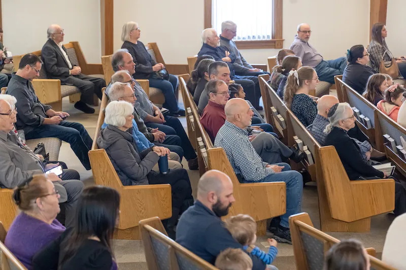 A diverse group of people seated in a church pew, listening attentively.