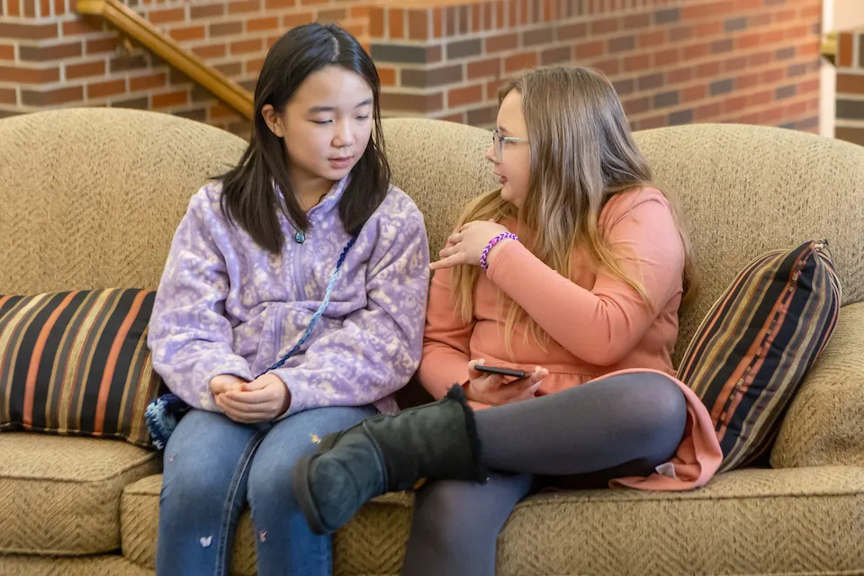 Two girls sitting on a couch talking.