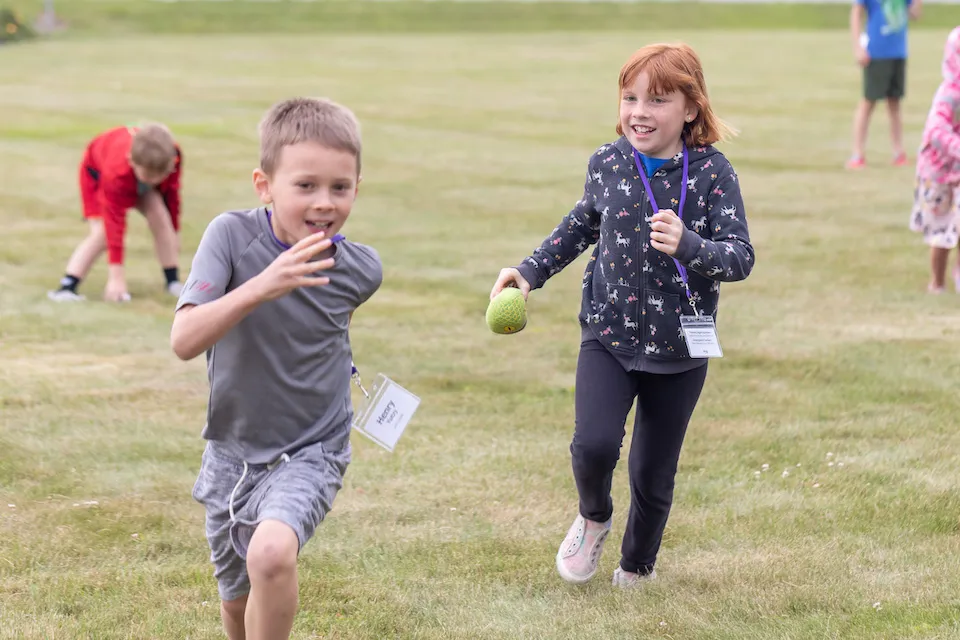 A boy and a girl running and playing on grass.