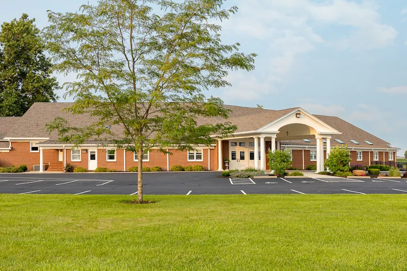 Shiloh Mennonite Church's brick building, surrounded by grass and trees, with a parking lot in front.