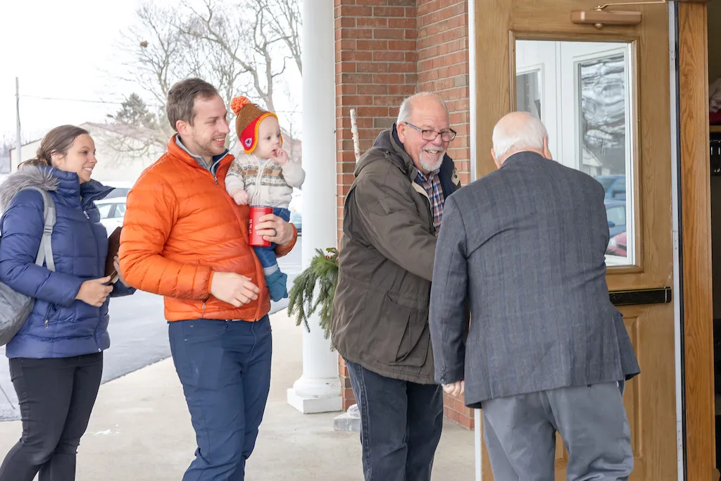 A family arriving at the church building; a man opens the door to let them in.