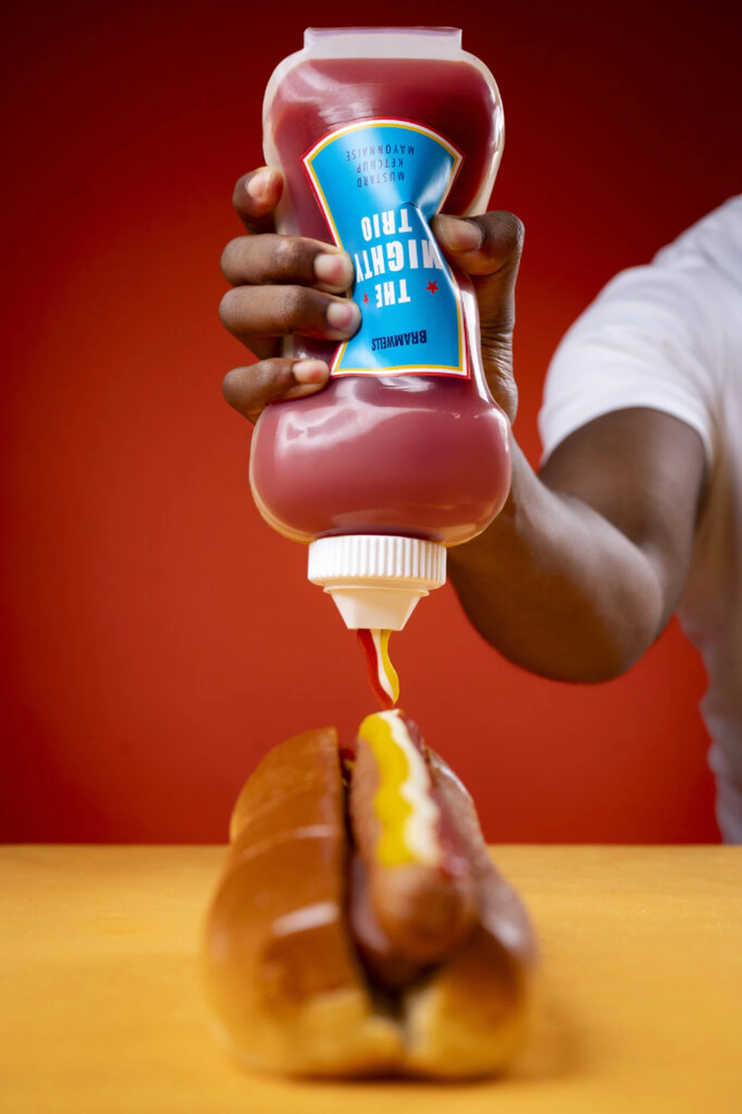 Bramwells triple-chamber bottle being squeezed to dispense ketchup, mayonnaise and mustard together