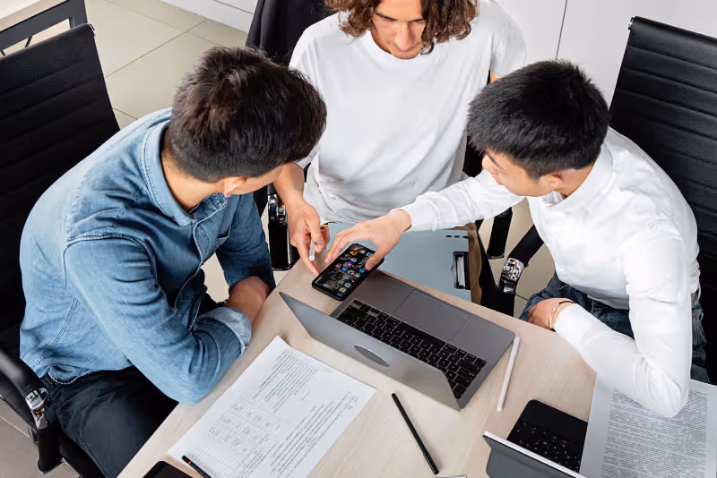 stock photo three people discussing at table over phone and laptop