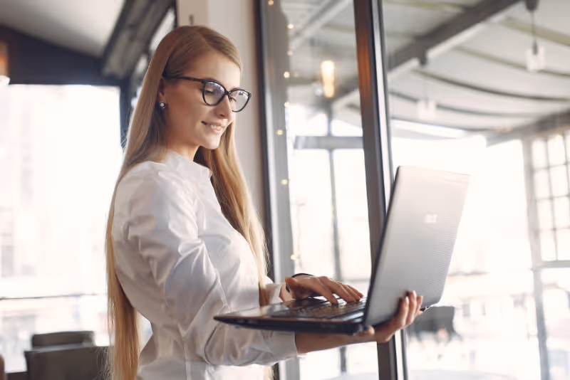 stock photo woman standing and holding laptop wile typing with one hand