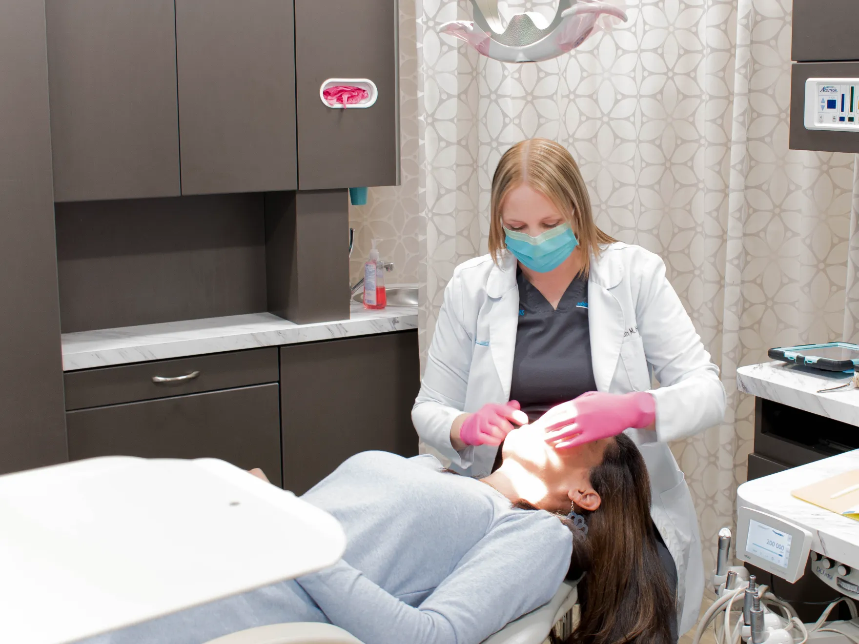 Dentist wearing a mask examines a patient's teeth in a dental office.