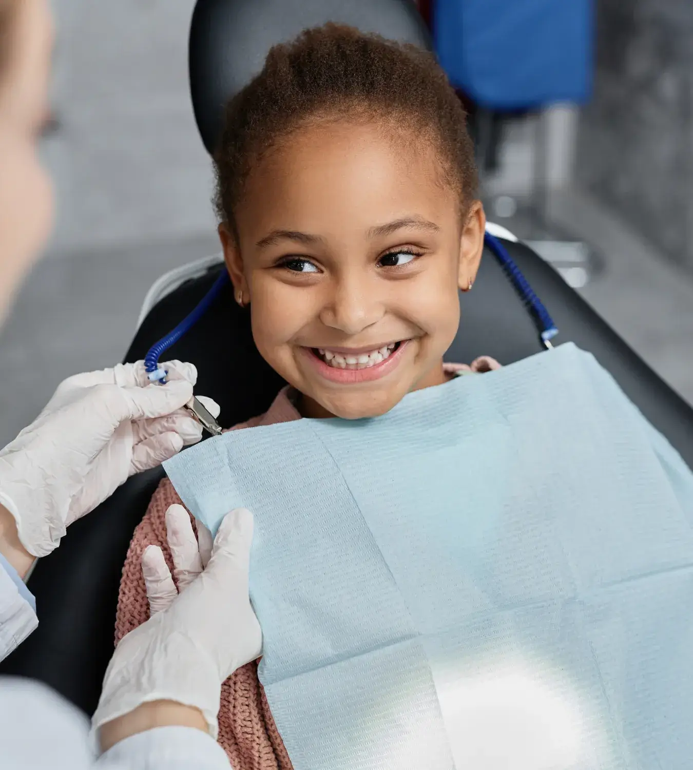 A child in a dental chair smiles as a dentist prepares for a check-up.