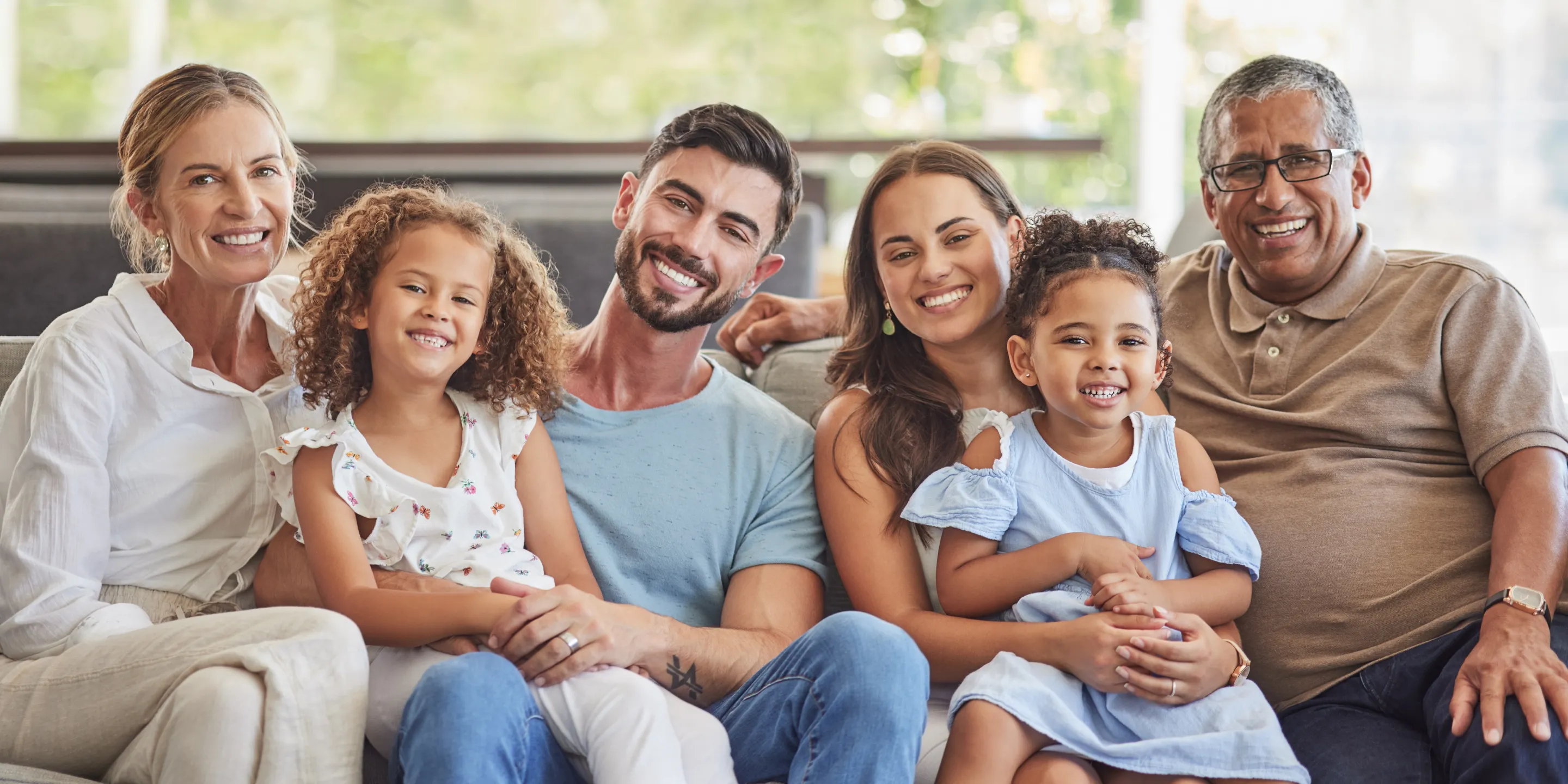 A happy family of six sits on a couch, smiling warmly at the camera.