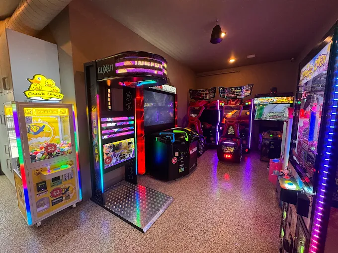 Indoor arcade room with colorful gaming machines and a claw machine labeled Duck Shop.