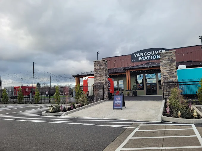 Exterior of Vancouver Station building with stone pillars, a ramp, and parked food trucks under a cloudy sky.