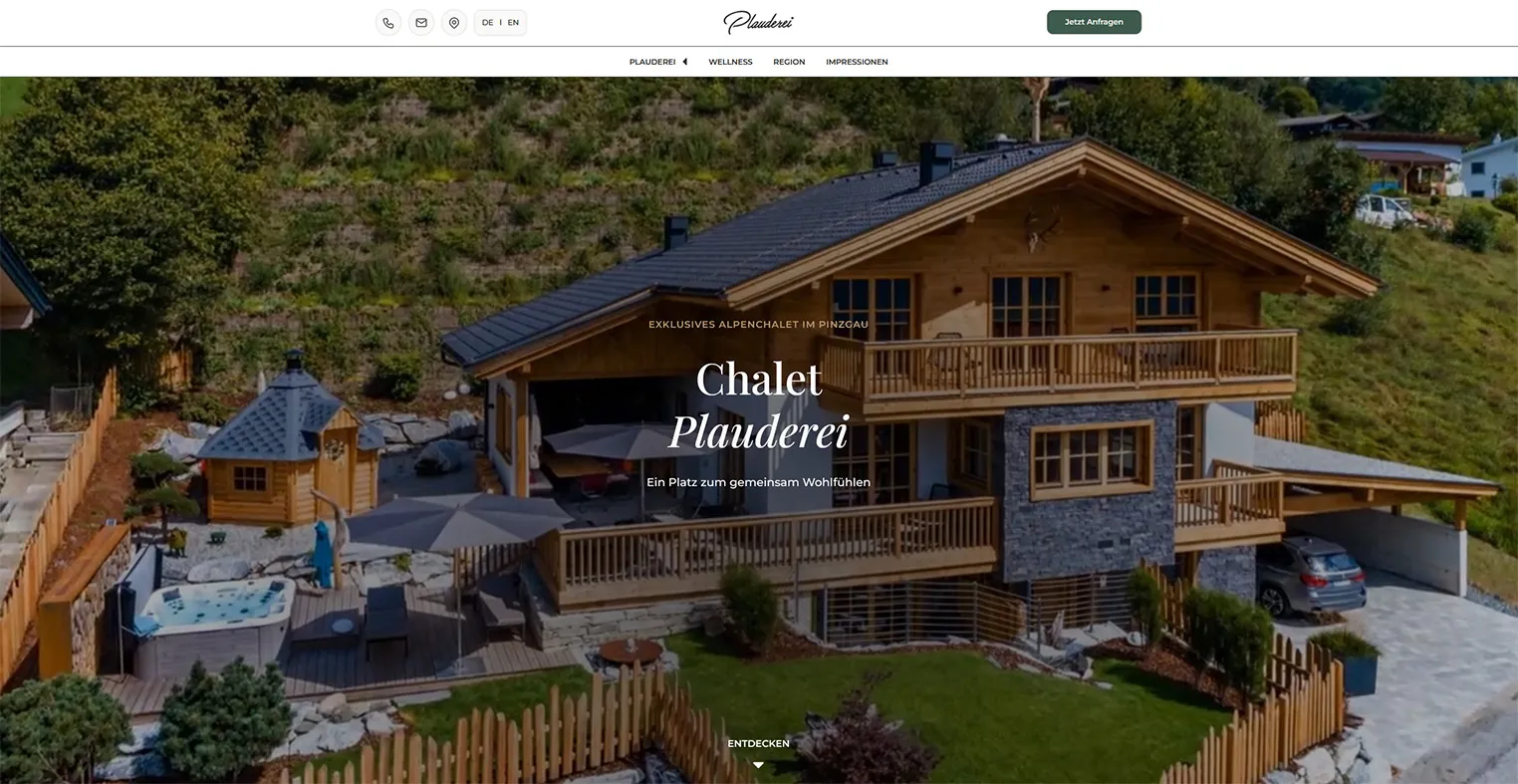 Modernes Holzchalet mit Terrasse, Whirlpool, Sonnenschirmen und umliegender Berglandschaft.