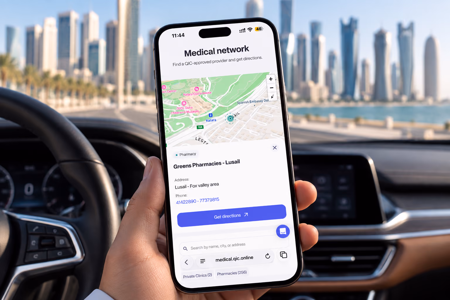 Smartphone held inside a car shows a medical network app with a map focused on Greens Pharmacies - Lusail, displaying address, phone number, and a 'Get directions' button, with city skyline blurred in the background.