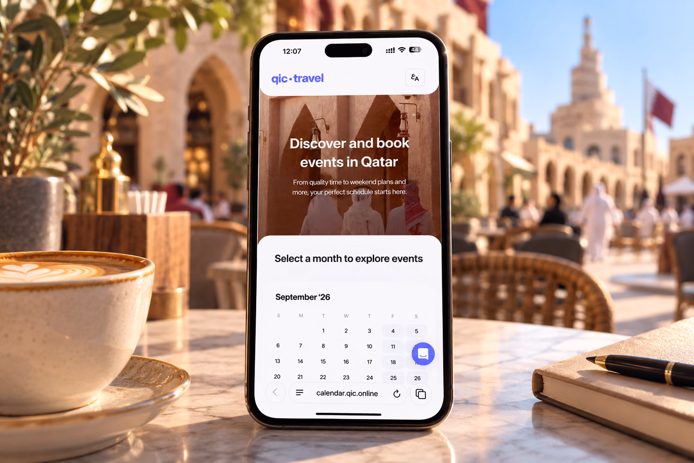 Smartphone on a table displaying a website to discover and book events in Qatar, showing a calendar for September 2026, with a cappuccino cup on the left and a notebook with a pen on the right, an outdoor café scene blurred in the background.