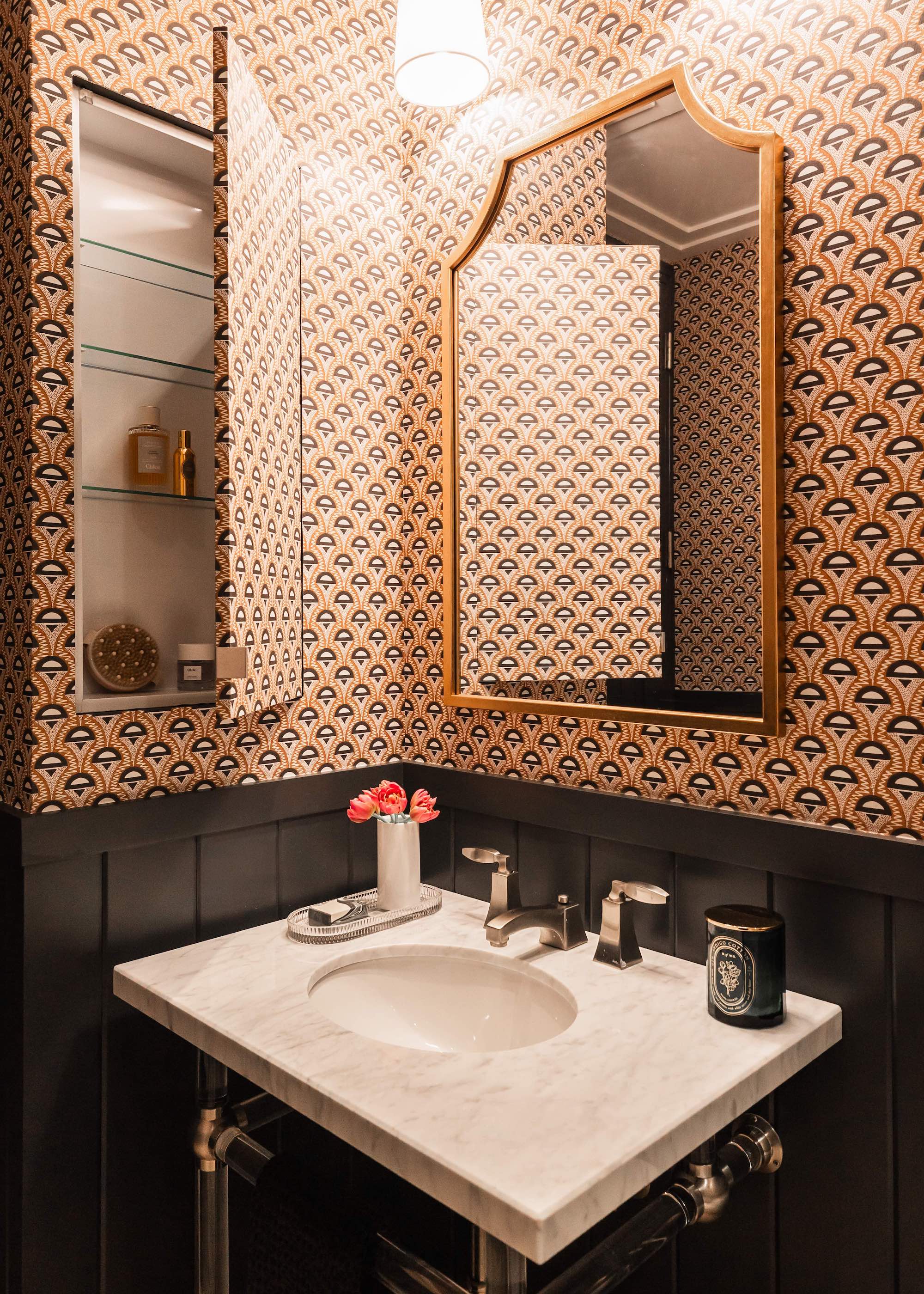 a small bathroom with wallpaper and hidden medicine cabinet on the left side. There is also a large mirror above the sink.